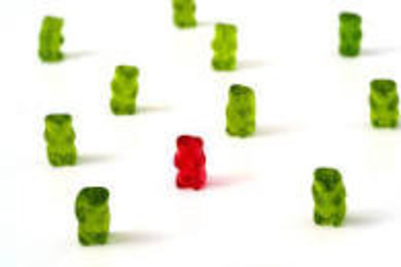 May include: A single red gummy bear surrounded by a group of green gummy bears.