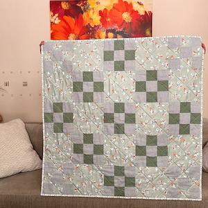 May include: A green and white checkered quilt with a floral pattern. The quilt is made of cotton fabric and has a white trim.