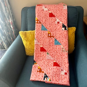 May include: A pink quilt with a geometric pattern of triangles and stars. The quilt is made of cotton fabric and has a soft, quilted texture.