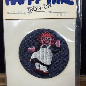 May include: A vintage "Happy Time" iron-on patch featuring a cartoon character with red hair, a white dress, and pink accents. The patch is on a dark blue circular background, packaged in a clear plastic sleeve with a price tag.