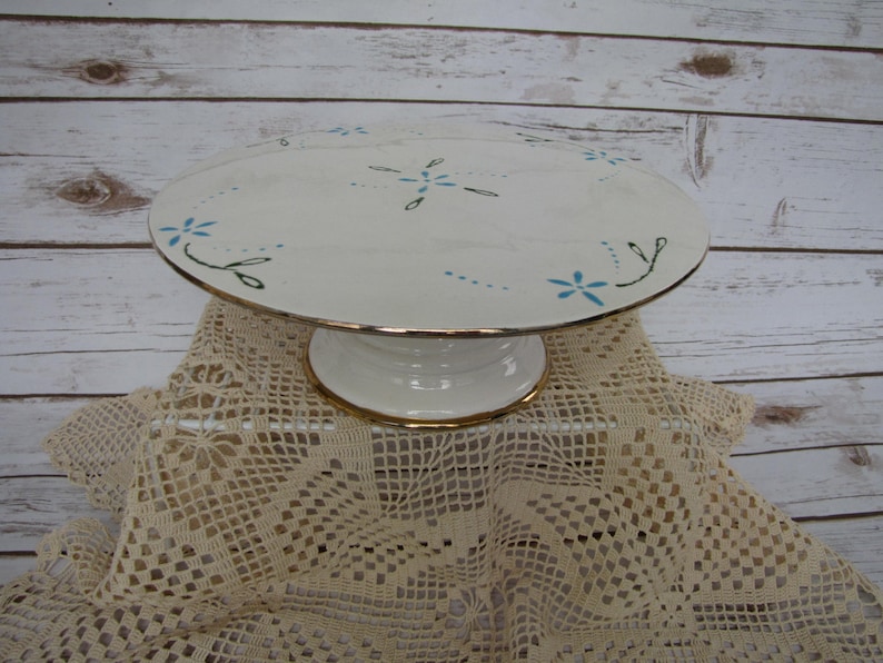 May include: White ceramic cake stand with a gold rim and blue and green floral design.