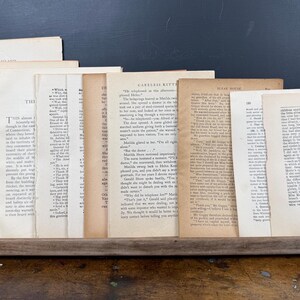 May include: A collection of aged book pages, some with visible text, arranged in a wooden frame. The pages display varying shades of cream and tan, suggesting age and use. The background is a dark chalkboard.