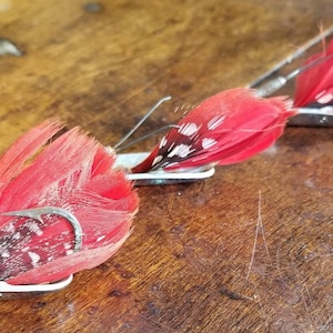 May include: Three red and white feather fishing lures with silver hooks and metal bases.