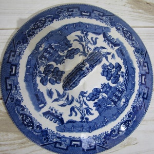 May include: Blue and white porcelain lid with a handle. The lid features a traditional Chinese willow pattern with a house, trees, and birds.