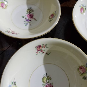 May include: Three white ceramic bowls with gold rims and floral designs. The bowls have a cream background with pink, blue, and green flowers.