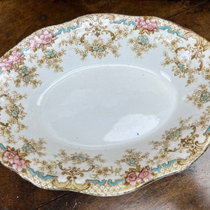 May include: A white oval serving dish with a blue and gold floral pattern. The dish has a scalloped edge and is decorated with pink and blue flowers.