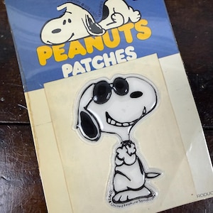 May include: Vintage Snoopy patches on a blue and yellow card. The patches feature Snoopy in sunglasses and the words "PEANUTS PATCHES". The card has a price tag of 98¢.