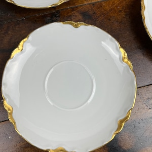 May include: White porcelain saucer with a gold rim and scalloped edge.