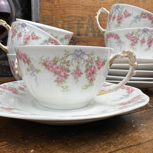 May include: A set of vintage teacups and saucers with a floral pattern. The cups and saucers are white with pink and blue flowers and a gold trim.