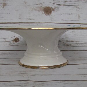 May include: White ceramic cake stand with a gold rim and a wide base. The stand is decorated with a blue and white floral pattern.