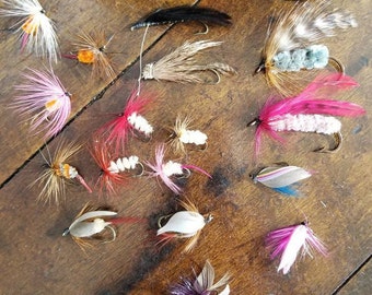 May include: A collection of 15 colorful fly fishing lures with feathers, fur, and beads. The lures are arranged on a wooden surface.