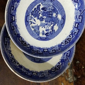 May include: Two blue and white porcelain plates with a traditional Chinese design. The plates feature a blue and white floral pattern with a central design of a pagoda and trees.