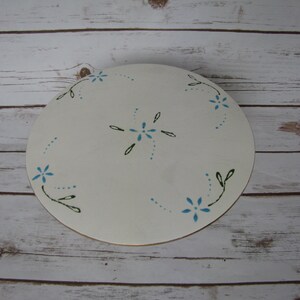 May include: White round cake stand with a blue and green floral design. The stand is made of wood and has a smooth surface.