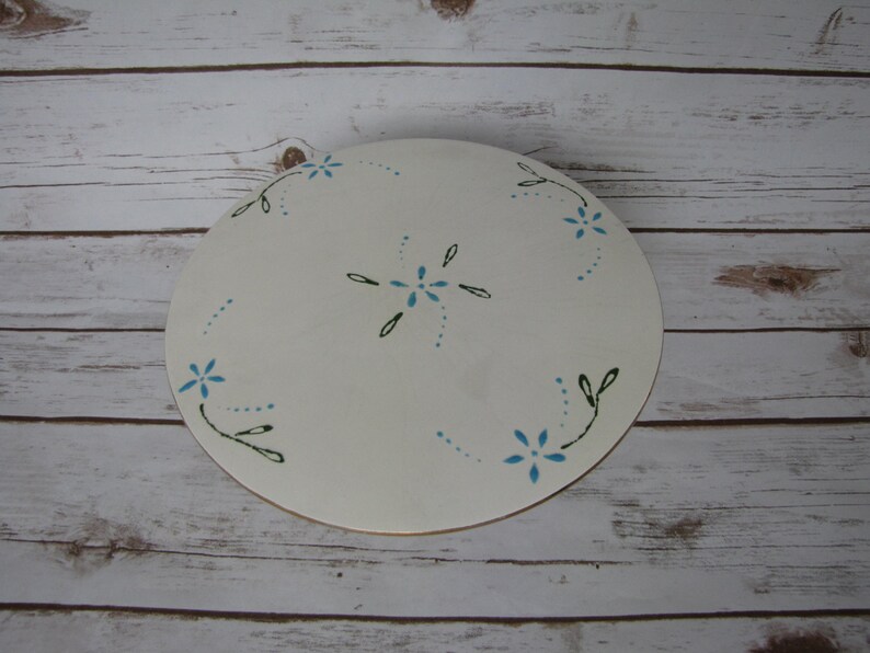 May include: White round cake stand with a blue and green floral design. The stand is made of wood and has a smooth surface.