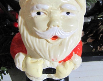 Op de afbeelding: Een wit plastic beeldje van Sinterklaas met een rode muts en een rood-wit pak. Hij heeft een witte baard en een rode neus.