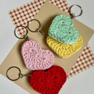 May include: Three crocheted heart-shaped keychains in pink, yellow, and red. The keychains are attached to silver key rings.