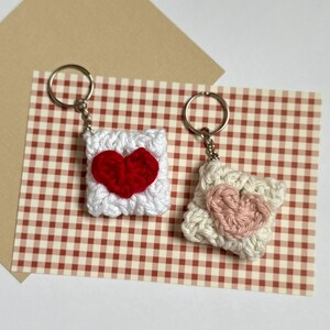 May include: Two crocheted heart-shaped keychains. One is white with a pink heart and the other is white with a red heart.