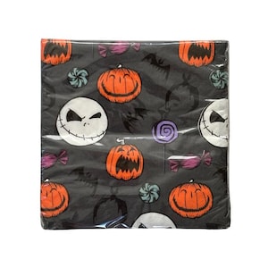 May include: A package of black Halloween-themed paper napkins. The napkins feature a repeating pattern of orange jack-o'-lanterns, Jack Skellington faces, bats, and candies in purple, teal, and pink. The napkins are wrapped in clear plastic.