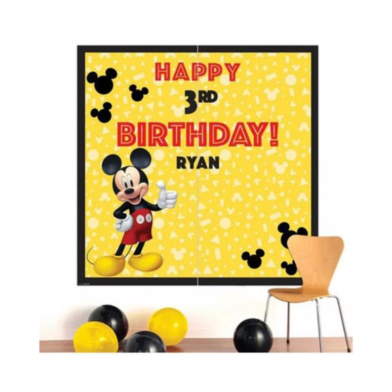 Puede incluir: Una pancarta de cumplea&ntilde;os amarilla con el texto "HAPPY 3RD BIRTHDAY! RYAN" y una imagen de dibujos animados de Mickey Mouse. Siluetas negras de Mickey Mouse est&aacute;n esparcidas alrededor de la pancarta. Globos negros y amarillos y una silla de madera est&aacute;n en primer plano.
