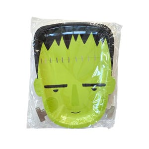 May include: A green paper plate shaped like Frankenstein's monster's face, with black hair and stitched details. The plate is in a clear plastic package, perfect for Halloween parties or themed events.
