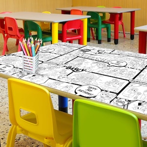 Op de afbeelding: Een zwart-wit kleurtafelkleed met een stripboekthema. Het tafelkleed heeft verschillende cartoonfiguren en de woorden "Happy 5th Birthday!" en "Awesome!" Het tafelkleed ligt op een tafel in een klaslokaal.