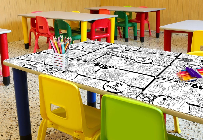 Op de afbeelding: Een zwart-wit kleurtafelkleed met een stripboekthema. Het tafelkleed heeft verschillende cartoonfiguren en de woorden "Happy 5th Birthday!" en "Awesome!" Het tafelkleed ligt op een tafel in een klaslokaal.