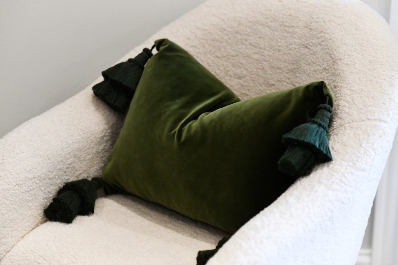 May include: A green velvet pillow with dark green tassels on a white fluffy chair.