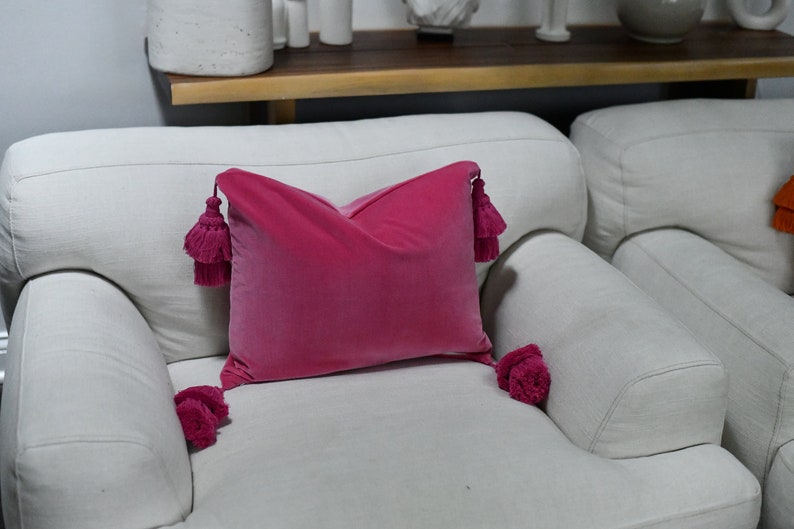 May include: A pink velvet throw pillow with tassels on a white couch.