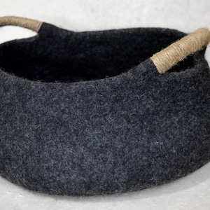 Könnte beinhalten: Ein dunkelgrauer Filz-Aufbewahrungskorb mit zwei Seilgriffen. Der Korb ist oval geformt und hat eine weiche, flauschige Textur.