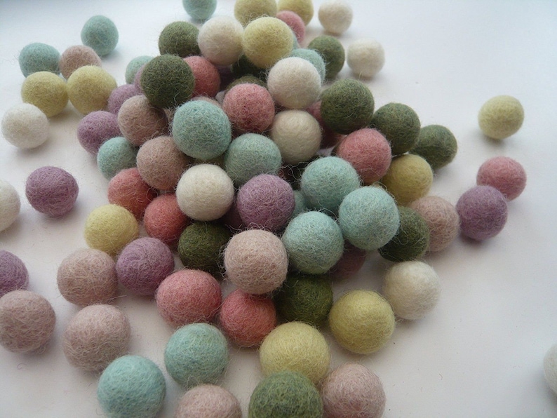 K&ouml;nnte beinhalten: Ein gro&szlig;er Haufen bunter Filzkugeln in verschiedenen Farbt&ouml;nen von Gr&uuml;n, Rosa, Lila, Beige und Wei&szlig;. Die Kugeln sind weich und flauschig, perfekt zum Basteln oder Dekorieren.
