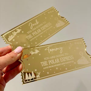 Pode incluir: Dois bilhetes dourados com um design de trem. Os bilhetes dizem "You are going to The Polar Express" e s&atilde;o personalizados com os nomes "Jack" e "Tommy".