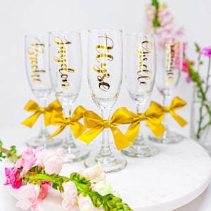 Personalized Champagne Flutes. These flutes feature Metallic Gold font with Gold bows. Font Style #5. Perfect for Bridesmaid Proposals, Birthdays, Weddings, and Special Events