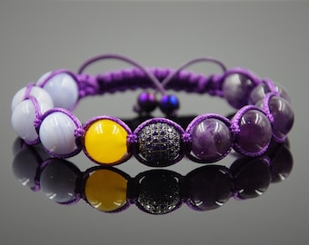 May include: A purple beaded bracelet with a yellow, blue, and purple stone design. The bracelet is made with a knotted cord.