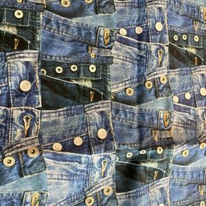 Puede incluir: Primer plano de una tela con un patrón repetitivo de parches de mezclilla azul. Los parches de mezclilla están dispuestos en un diseño de patchwork y presentan detalles de costura y botones visibles.