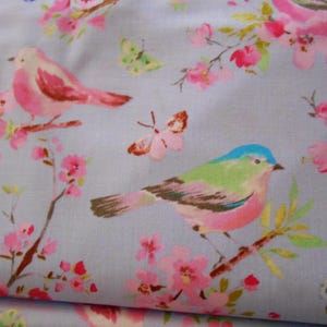 Op de afbeelding: Een lichtblauwe stof met een roze en groen bloemenpatroon met roze en blauwe vogels en vlinders.