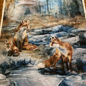 Può includere: Tessuto di cotone con un'illustrazione in stile acquerello di una famiglia di volpi in un ambiente forestale. L'immagine mostra tre volpi, con il testo "FOX DEN" e altri dettagli in basso. Il tessuto è 100% cotone.