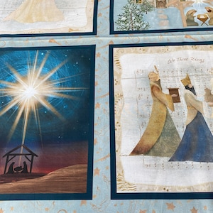 Op de afbeelding: Een stoffen paneel met vier religieuze illustraties. De afbeeldingen tonen een engel, een kerk in een besneeuwd landschap, de geboorte en de drie wijzen met de tekst "We Three Kings". De achtergrond is lichtblauw met muzieknoten en sterren.