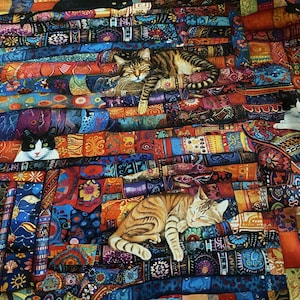 Könnte beinhalten: Ein Stoffquilt mit einem lebendigen, mehrfarbigen Patchwork-Muster mit verschiedenen geometrischen und floralen Motiven. Mehrere Katzen sind auf dem Stoff abgebildet, darunter eine schwarze Katze, eine getigerte Katze und eine schwarz-weiße Katze.