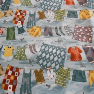 Könnte beinhalten: Ein blauer und weißer Stoff mit einem sich wiederholenden Muster von Kleidung, die an einer Wäscheleine hängt. Die Kleidung ist in verschiedenen Farben und Mustern, darunter Karos, Punkte und Streifen.