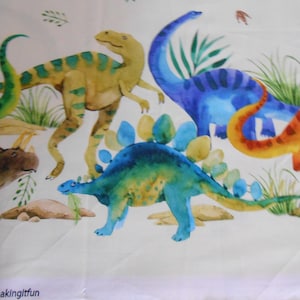 Könnte beinhalten: Ein weißer Stoff mit einem bunten Dinosaurier-Druck. Die Dinosaurier sind grün, blau, orange und braun. Der Stoff hat einen Rand mit dem Text "Border #makingitfun".