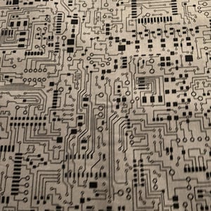 Könnte beinhalten: Nahaufnahme eines Stoffes mit einem schwarz-weißen Leiterplattenmuster. Das Muster weist komplizierte Linien, Quadrate und Rechtecke auf, die eine komplexe, technologische Ästhetik erzeugen. Der Hintergrund ist hellgrau.