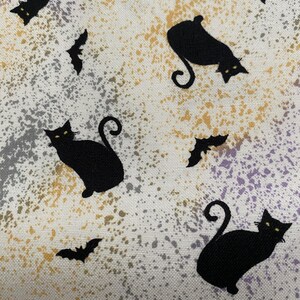 Könnte beinhalten: Ein Halloween-Stoff mit schwarzen Katzen-Silhouetten und Fledermausformen auf einem gesprenkelten Hintergrund. Der Hintergrund hat eine Mischung aus Weiß, Grau, Gelb und Lila.