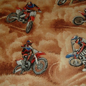 Op de afbeelding: Een bruine stof met een herhalend patroon van motocrossrijders op crossmotoren. De rijders dragen kleurrijke helmen en racepakken. De motoren zijn rood, blauw en zwart.