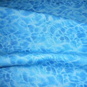 Könnte beinhalten: Ein blauer Stoff mit einem wasserartigen Muster. Der Stoff hat eine gewellte Textur und eine hellblaue Farbe.