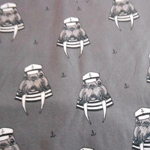 Può includere: Un tessuto grigio con un motivo ripetitivo di caricature di trichechi che indossano cappelli da marinaio. I trichechi indossano tutti cappelli da marinaio bianchi con una fascia nera e hanno occhi neri e baffi neri.