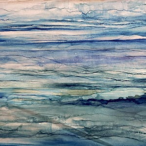 Op de afbeelding: Abstracte stof met een aquarelontwerp in tinten blauw, teal en beige. Het patroon heeft horizontale lijnen en kleurwashes, waardoor een vloeiend, oceaanachtig effect ontstaat. De stof is waarschijnlijk katoen of een vergelijkbaar materiaal.