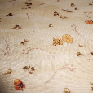 May include: A beige fabric with a beach-themed pattern. The fabric features seashells, starfish, sand dollars, and footprints.
