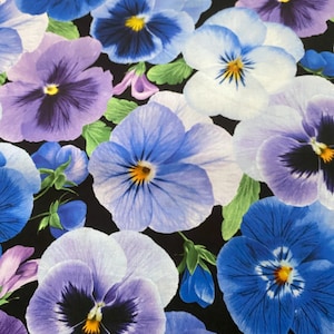 Op de afbeelding: Een close-up van een stof met een bloemenpatroon met viooltjes in tinten blauw, paars en wit tegen een zwarte achtergrond. De viooltjes hebben gele centra en groene bladeren.