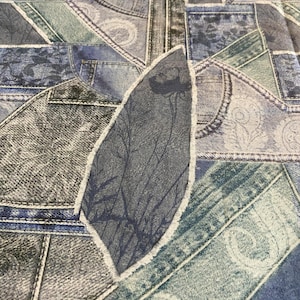 Könnte beinhalten: Ein Patchwork-Textil mit verschiedenen Denim-Stücken in Blau-, Grau- und Grüntönen. Das Design beinhaltet verschiedene Denim-Texturen, darunter Taschen, Nähte und dekorative Muster. Ein blattförmiges Stück mit einem Baumzweig-Design ist ebenfalls vorhanden.
