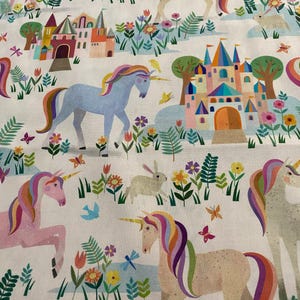 Puede incluir: Un diseño de tela caprichoso con unicornios con crines y colas de arcoíris, sobre un fondo de castillos coloridos, flores, mariposas y un conejo. Los unicornios son de color rosa, azul y beige, creando una escena de cuento de hadas.